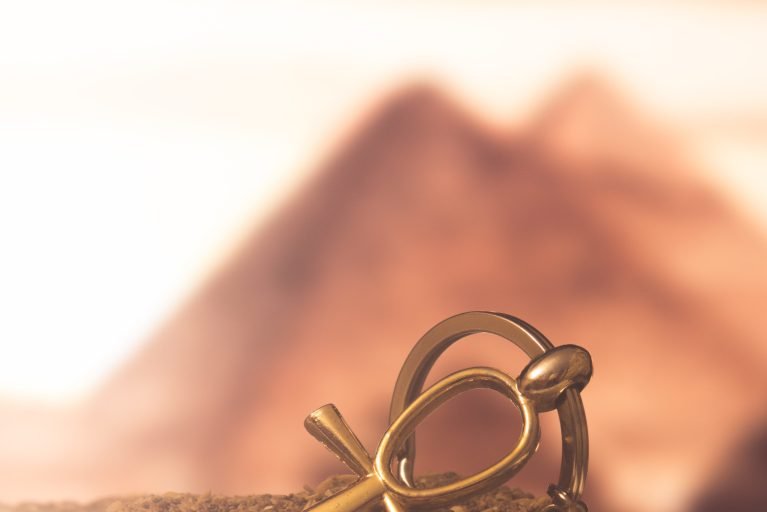 The Egyptian ankh is a cross in the sand against the backdrop of the Great Pyramids. Photo toned.