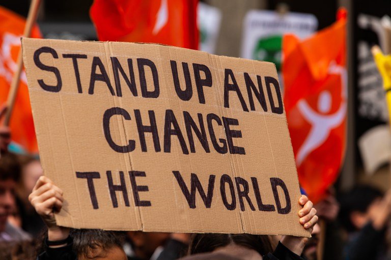 A cardboard sign is seen close up, saying stand up and change the world, as eco-activists march for the environment on a street in Montreal, Canada